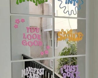 May include: A set of six square wall mirrors arranged in a grid. Each mirror features colorful vinyl lettering: green text reading DON'T CHASE ATTRACT, blue text THAT'S HOT, pink text YOU LOOK GOOD, orange text SMILE, white text MANIFEST AND WORK HARD, and purple text I JUST DON'T CARE.