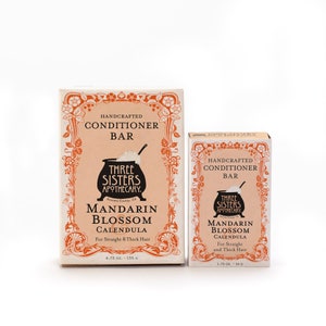 May include: Two boxes of handcrafted conditioner bars from Three Sisters Apothecary. The boxes are peach colored with a floral border and feature a black and white illustration of a cauldron. The text on the boxes reads "Handcrafted Conditioner Bar" and "Mandarin Blossom Calendula". The smaller box is 1.75 ounces and the larger box is 4.75 ounces.