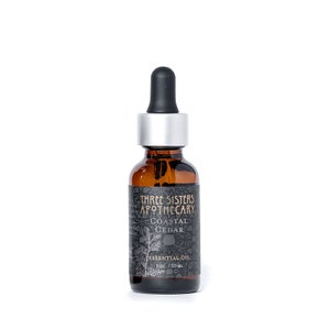 May include: A brown glass bottle with a silver cap and dropper. The bottle is labeled "Three Sisters Apothecary Coastal Cedar Essential Oil 1 oz. / 30 ml."