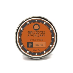 May include: A round, silver tin with a black and white label. The label reads "Three Sisters Apothecary" and "shave soap" in a black font. The label also features a small illustration of a cauldron and the words "bay rum" in a white font. The tin is 3.5 oz or 99 g.