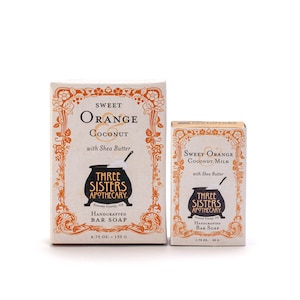 May include: Two boxes of handmade bar soap from Three Sisters Apothecary. The larger box is labeled "Sweet Orange & Coconut with Shea Butter" and the smaller box is labeled "Sweet Orange Coconut Milk with Shea Butter". Both boxes feature a vintage-inspired design with a black cauldron and floral accents.