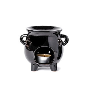 May include: Black ceramic cauldron oil burner with a small tea light candle inside. The cauldron has three legs and two handles. There are star cutouts on the sides.