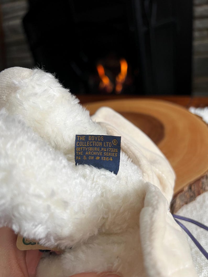 Pode incluir: Um close-up de um brinquedo de pel&uacute;cia creme com uma etiqueta azul. A etiqueta diz "THE BOYDS COLLECTION LTD" e inclui texto sobre Gettysburg, PA, e a s&eacute;rie Archive. O brinquedo de pel&uacute;cia &eacute; macio e fofo.