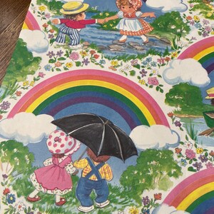 May include: A vibrant illustration with children, rainbows, and clouds. One scene shows two children crossing a stream, while another depicts two children under an umbrella. The artwork is framed by rainbows and floral details.
