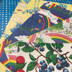 May include: A selection of colourful vintage paper sheets with diverse patterns. Designs include a blue polka dot pattern, a yellow floral pattern with a girl, a rainbow with clouds, and a branch of blueberries and cherries.