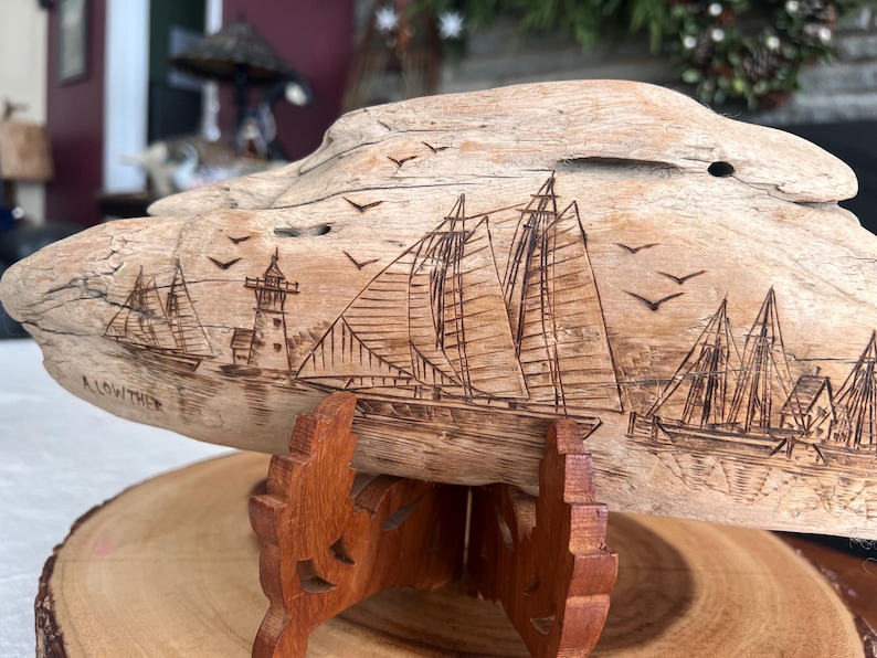 May include: A wooden sculpture of a nautical scene, featuring sailboats, a lighthouse, and flying birds. The artwork is carved into a piece of driftwood and mounted on a wooden stand. The sculpture is displayed on a wooden slice.
