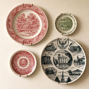 Może przedstawiać: Cztery talerze dekoracyjne z historycznymi scenami. Dwa talerze mają czerwono-białe wzory, jeden z krajobrazem, a drugi z centralnym obrazem budynku. Zielono-biały talerz przedstawia budynek, a czarno-biały talerz prezentuje różne budynki i zabytki.