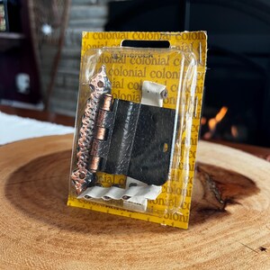 Puede incluir: Un paquete de bisagras de puerta de estilo colonial. Las bisagras son negras y color cobre, con un diseño decorativo. El embalaje amarillo tiene la palabra "colonial" impresa.