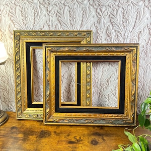 May include: Two rectangular picture frames with ornate gold and dark grey carved edges. Each frame features a deep black velvet inner border and a thin wire hanging mechanism attached to the back, visible through the open center of the frames.