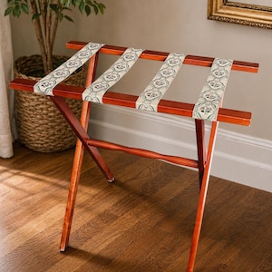 Puede incluir: Un estante de equipaje de madera con un cálido acabado marrón rojizo. El estante presenta correas decorativas con un fondo crema y un patrón floral en rojo, verde y negro. El estante está diseñado para sostener equipaje y es de madera. Mide 76 cm de largo.