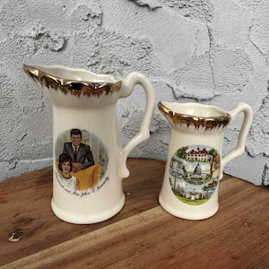 May include: Two white ceramic pitchers with gold trim. One pitcher features a portrait of John F. Kennedy and his wife, with the text "President and Mrs. John F. Kennedy." The other pitcher displays a Washington D.C. scene.