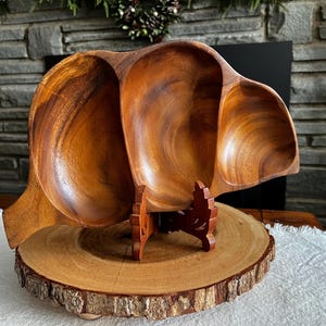 Puede incluir: Un cuenco de madera para servir de tres secciones con un acabado de vetas de madera natural. El cuenco está sostenido por un soporte de madera decorativo y se asienta sobre una base de madera redonda. Ideal para servir aperitivos.