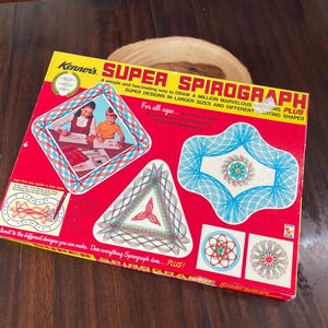 May include: A vintage Kenner's Super Spirograph set in a red box. The box features illustrations of Spirograph designs and children using the toy. Text on the box includes "A simple and fascinating way to draw a million marvelous patterns plus."