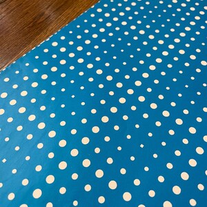 May include: A close-up of a blue surface with a pattern of white polka dots. The dots are of varying sizes and evenly spaced. The background is a dark wood grain.