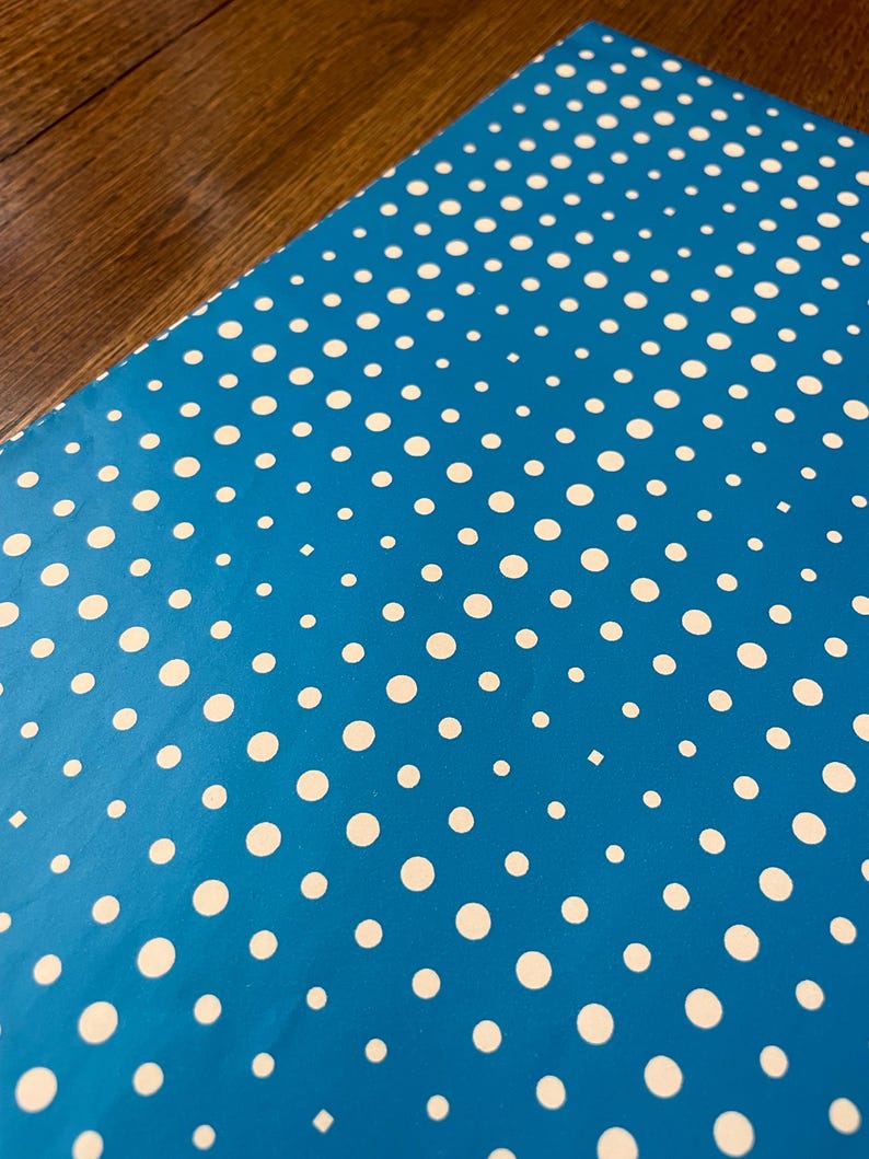 May include: A close-up of a blue surface with a pattern of white polka dots. The dots are of varying sizes and evenly spaced. The background is a dark wood grain.