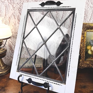 May include: A white rectangular wooden frame featuring a diamond-patterned leaded glass insert. The frame includes two black metal handles attached to the top and bottom edges, and it is supported by a black metal display stand.
