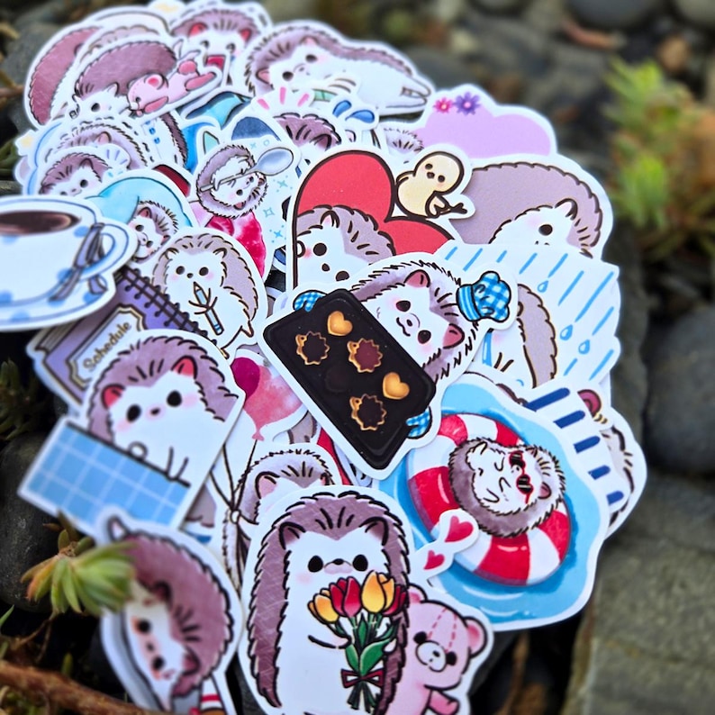May include: A collection of colorful stickers featuring cute cartoon hedgehogs in various activities, including baking, swimming, and holding flowers. The stickers are printed on white paper and have a glossy finish.