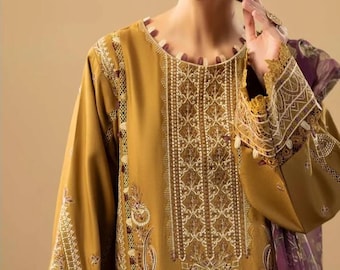 May include: Mustard-colored long-sleeved tunic with intricate white and brown embroidery. The tunic features detailed patterns on the sleeves and bodice, with a purple scarf visible on the side. The neckline is trimmed with a decorative border.