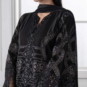 May include: Black embroidered tunic with detailed patterns and sequin embellishments. The long-sleeved top has sheer lace detailing on the sleeves and a matching scarf. The outfit is a formal wear ensemble.
