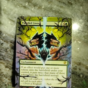 May include: A Magic: The Gathering card with a green, yellow, and blue background. The card is titled "Parallel Lives" and is an enchantment. The card text reads: "If an effect would put one or more tokens onto the battlefield under your control, it puts twice that many of those tokens onto the battlefield instead." The card also features a quote from the character Ulrich of Krallenhorst: "There will come a time when the only left will be each other."