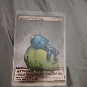 May include: A trading card featuring the artwork of a blue robot with a green, bulbous body. The card is titled "Solemn Simulacrum" and includes game text. The card is encased in a protective sleeve.
