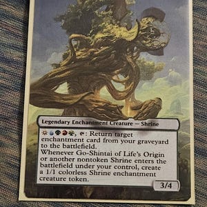 May include: A Magic: The Gathering card titled "Go-Shintai of Life's Origin." The card features a detailed illustration of a tree-like structure with a light blue sky background. The card text describes its abilities and stats.