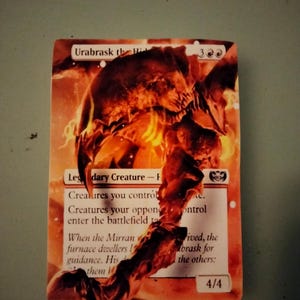 May include: A fantasy trading card featuring a fiery red and orange creature with a skull-like head. The card is titled "Urabrask the Hind" and has a power and toughness of 4/4. The card text reads "Legendary Creature - Phyrexian".
