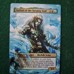 May include: A blue and green fantasy-style trading card with a white, blue, and gold creature on it. The card is titled "Hakbal of the Surging Soul" and has the text "Legendary Creature - Merfolk Scout". The card has a power and toughness of 3/3.