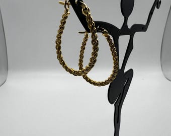May include: A pair of gold-toned hoop earrings with a twisted rope design. The earrings are displayed on a black metal earring stand.