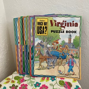 May include: A stack of colorful children's puzzle books with the title "Which Way USA? Virginia Puzzle Book" on the front cover. The cover features an illustration of a horse-drawn carriage with people in colonial clothing.