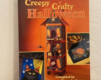 May include: A book titled "Creepy Crafty Halloween" with a colorful cover featuring a three-tiered house, a black cat with a witch's hat, and a pumpkin-shaped table runner.