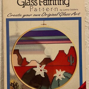 Peut inclure: Patron de peinture sur verre pour une sc&egrave;ne de lune du d&eacute;sert. Le motif repr&eacute;sente un coucher de soleil rouge, orange et bleu sur un paysage d&eacute;sertique avec des cactus et des fleurs blanches. Le motif est dans un cercle de 35,5 cm. Le motif est de Lanna Siddens et est de Plaid.