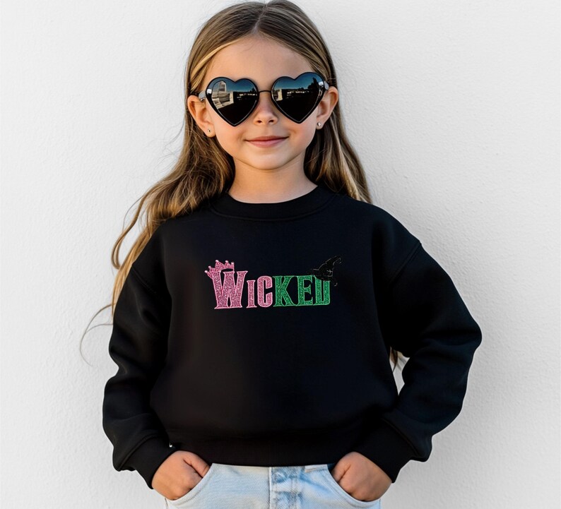 May include: Black sweatshirt with the word "Wicked" in pink and green glitter lettering. A crown graphic is above the word "Wicked". The sweatshirt is worn by a young person wearing heart-shaped sunglasses.