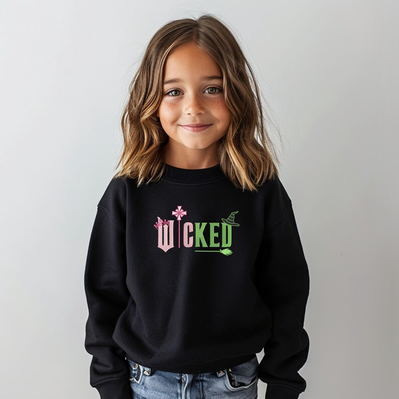 May include: A black sweatshirt with a pink and green graphic that says "WICKED" with a witch's hat, a wand, and a broom.
