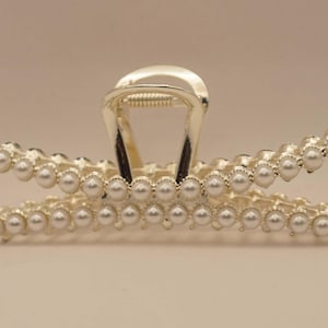 Puede incluir: Pinza para el cabello plateada adornada con hileras de perlas de imitación. La pinza presenta un diseño clásico de garra con un mecanismo de resorte para una sujeción segura. Este elegante accesorio para el cabello es adecuado para varios peinados.