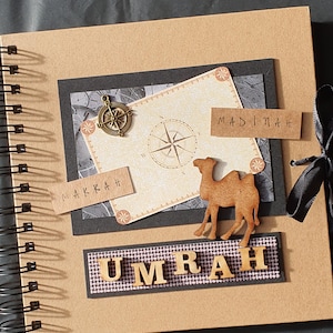 May include: A brown scrapbook with a black ribbon and a compass, a camel, and the words "UMRAH", "MAKKAH", and "MADINA" on the cover.