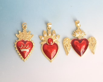 May include: Three gold-colored pendants with red heart-shaped centers. The pendants feature intricate designs, including crowns, gems, and wings. The pendants are likely for necklaces or other jewelry.