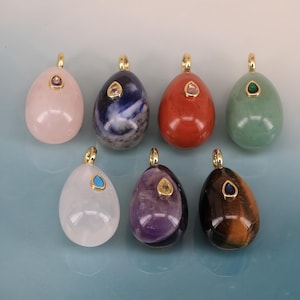 May include: Seven egg-shaped pendants made of various polished gemstones, including rose quartz, sodalite, red jasper, green aventurine, clear quartz, amethyst, and tiger's eye. Each pendant features a gold-toned bail and a small teardrop-shaped gemstone inlay.