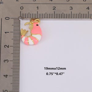 May include: A gold-toned shrimp charm with pink, white, and gold enamel detailing. The charm measures 0.75" x 0.47" (19mm x 12mm). The shrimp has a curved body with striped white and pink sections, and gold accents.