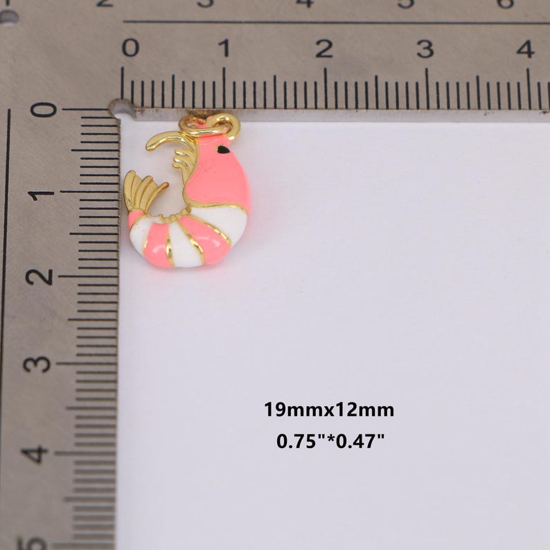 May include: A gold-toned shrimp charm with pink, white, and gold enamel detailing. The charm measures 0.75" x 0.47" (19mm x 12mm). The shrimp has a curved body with striped white and pink sections, and gold accents.