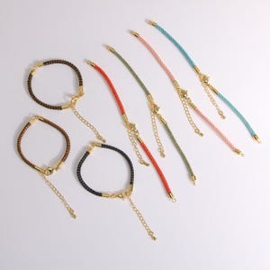May include: A collection of colorful bracelets with gold-toned clasps and extenders. The bracelets feature braided cords in various colors, including brown, black, red, green, pink, and blue. Each bracelet has a decorative charm.