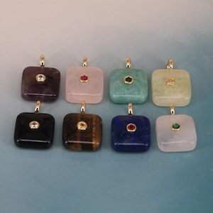 May include: Eight square-shaped gemstone pendants arranged in two rows. Each pendant features a gold-tone bail and a small, round, bezel-set accent stone in the centre. The stones include purple, pink, green, yellow, black, brown, blue, and white.