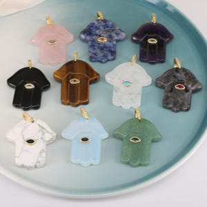 Può includere: Una collezione di dieci ciondoli a forma di mano di Hamsa realizzati in varie pietre preziose, tra cui quarzo rosa, sodalite, ametista, onice nero, occhio di tigre, quarzo chiaro, marmo grigio, howlite bianca, opalite e avventurina verde, con gancio dorato.
