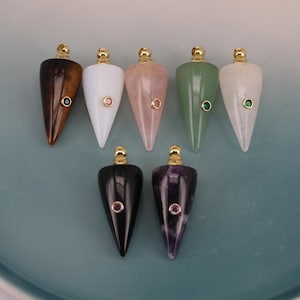 May include: Seven cone-shaped pendants made of various polished stones, including brown, white, pink, green, and black varieties. Each pendant features a gold-toned metal cap at the top and a small, circular gemstone inlay on the front surface.