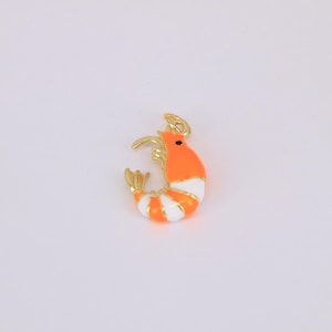 May include: A gold-colored shrimp charm with orange and white stripes. The shrimp has a small black eye and a gold-colored hook at the top for attaching to a necklace or bracelet. The charm is a cute and whimsical accessory.