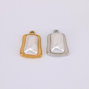 May include: Two pendant charms. One is gold-toned with a white, rectangular center. The other is silver-toned with a white, rectangular center. Both have a small loop at the top for attaching to a chain or other jewelry component.