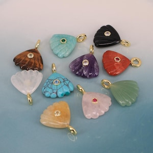 May include: A collection of gemstone pendants in various colors, including brown, turquoise, amethyst, red, and green. Each pendant has a fan-like shape with a gold-colored bail and a small gemstone or crystal accent in the center.