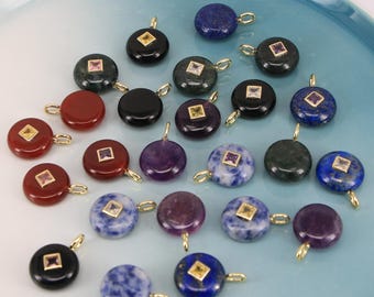 Puede incluir: Una colección de colgantes de piedras preciosas en varios colores, incluyendo rojo, negro, morado, azul y verde. Cada colgante presenta una pequeña gema de corte cuadrado en el centro y un lazo dorado para colgar.