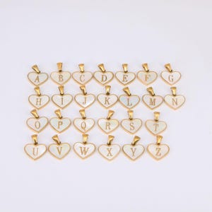 May include: A selection of heart-shaped pendants, each displaying a letter from A to Z. The pendants have a gold-coloured frame and a white, pearlescent centre. A stylish and personalised jewellery item.