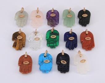 May include: A collection of Hamsa hand pendants in various colors and materials, including green jade, rose quartz, amethyst, and tiger's eye. Each pendant features a gold-colored bail and an eye-shaped accent.